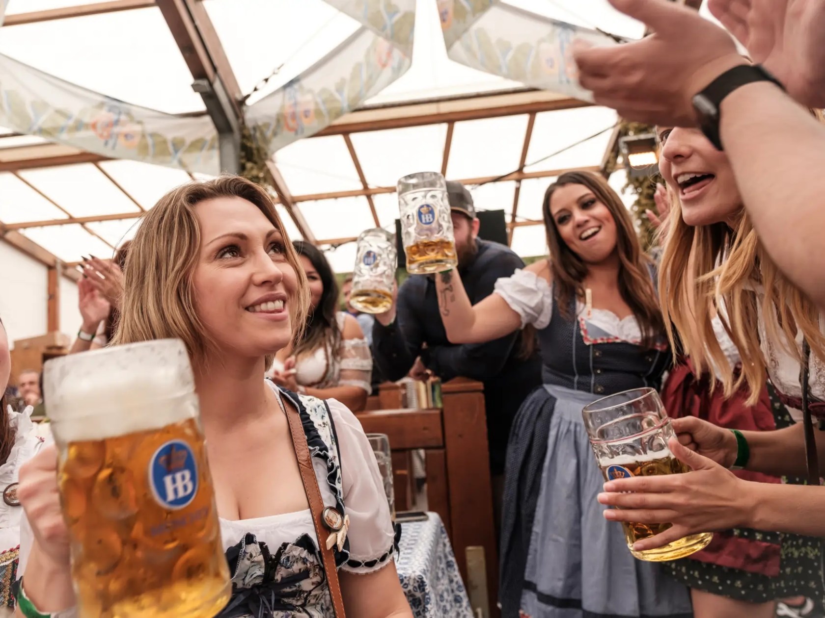 People in traditional attire raise beer mugs and celebrate at a festive indoor gathering.