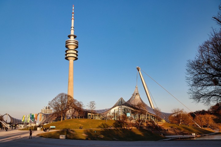 Tall tower beside modern tent-like structure in park under clear blue sky.