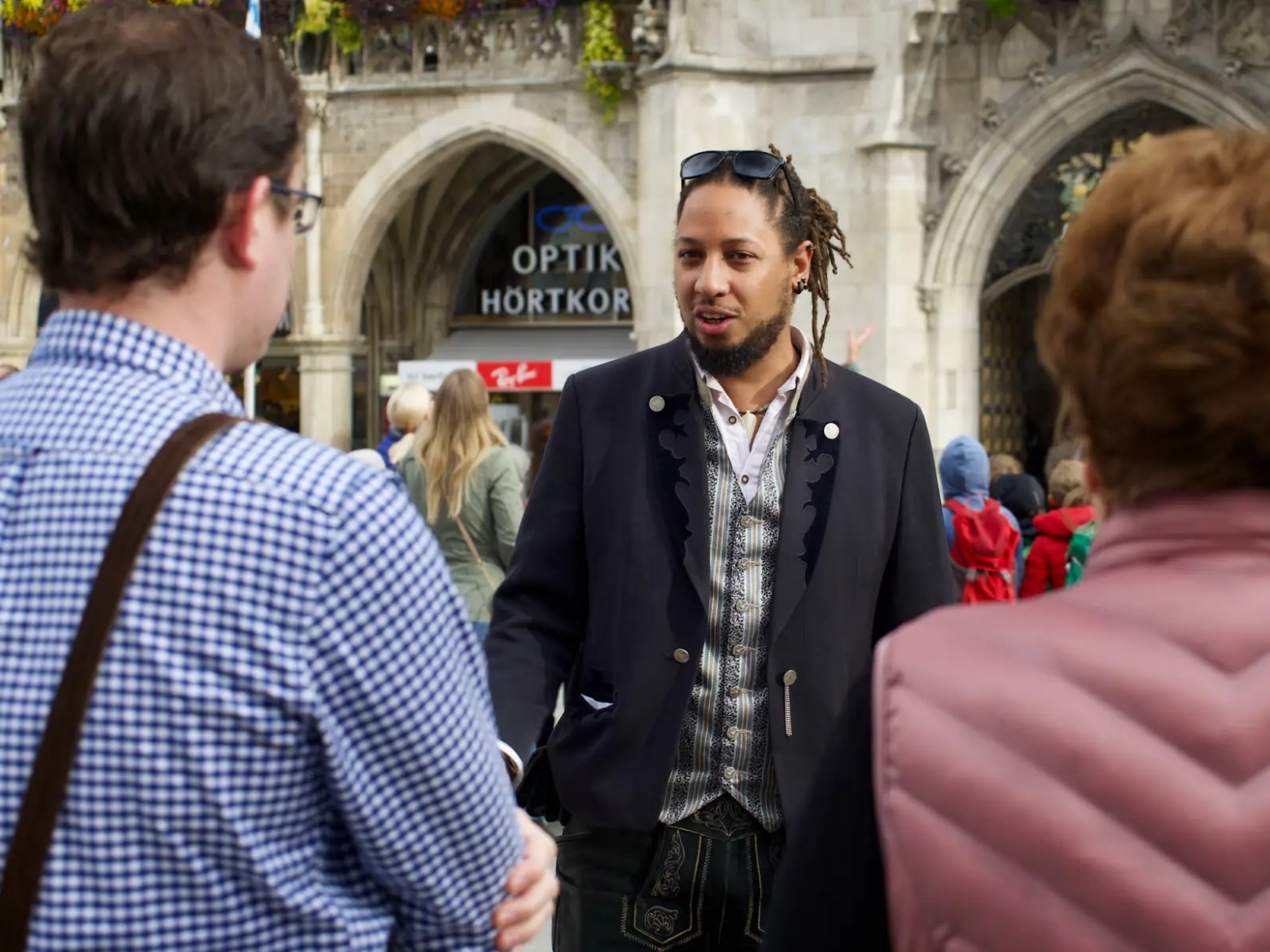 Man speaking to two people outdoors, near ornate building.