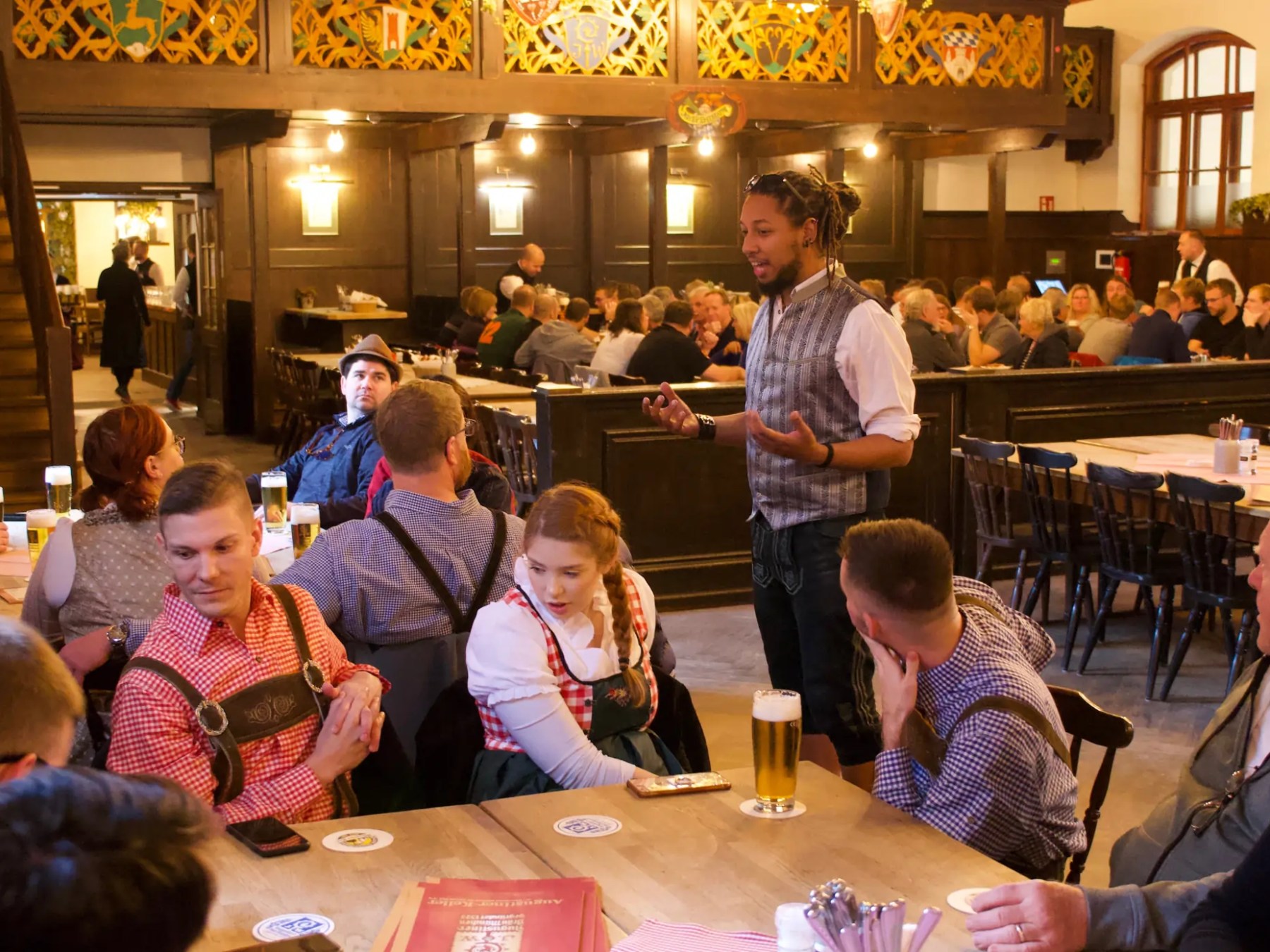 Man speaking to a group in a traditional pub setting with people in lederhosen.