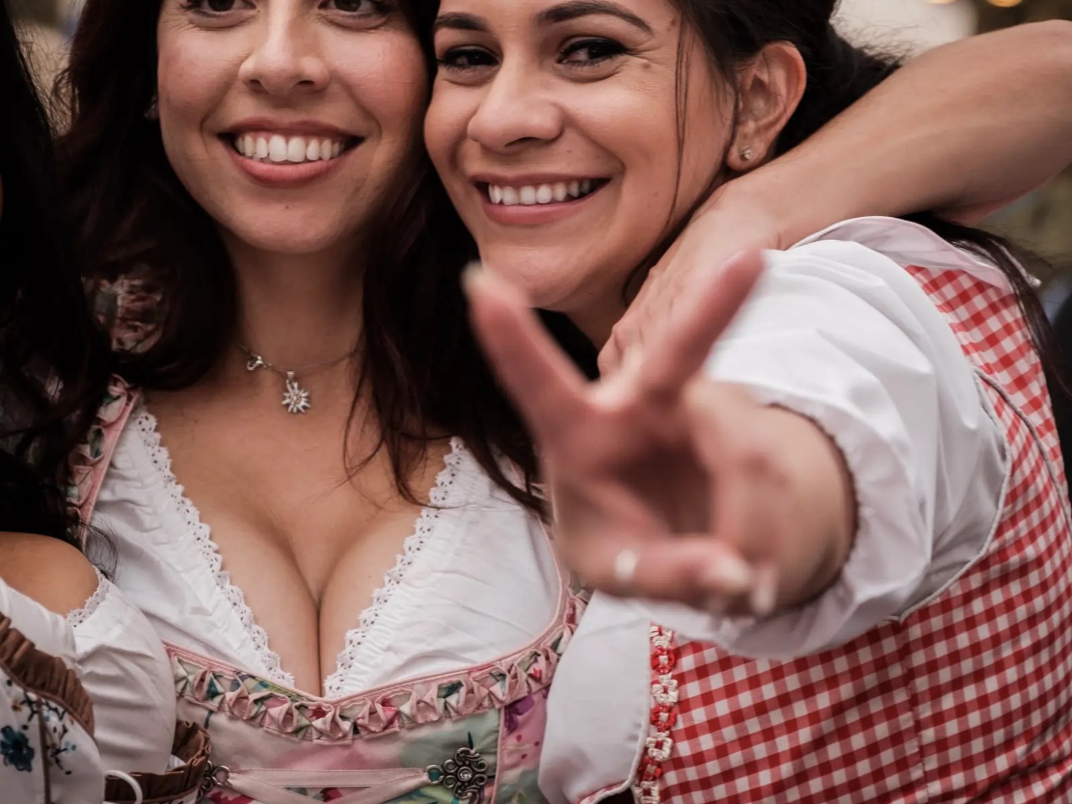 Two smiling women in traditional dresses pose with a peace sign.