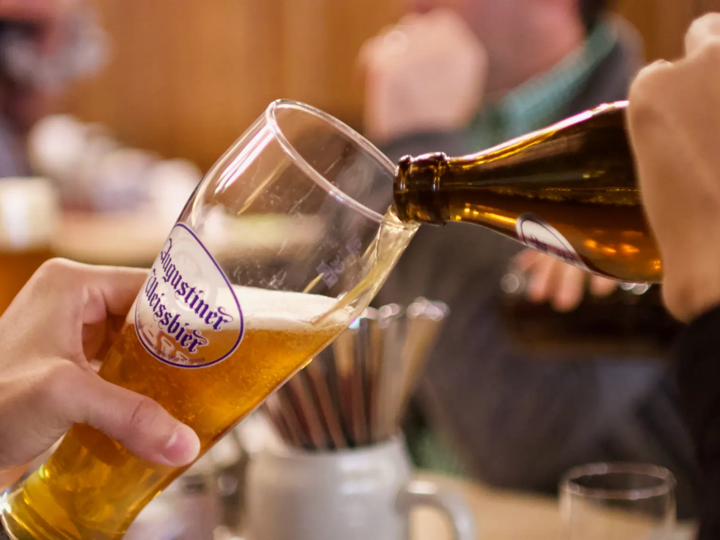 Person pouring beer from bottle into glass at a table.
