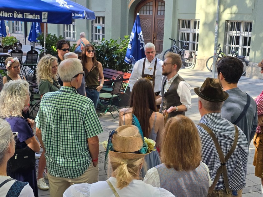 A group of people gathered outdoors under blue umbrellas, some wearing traditional outfits.