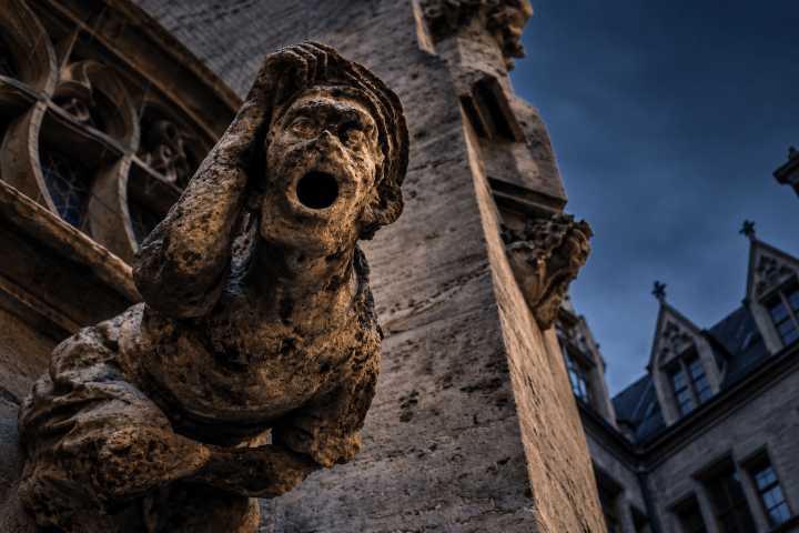 Stone gargoyle on building facade with dramatic clouds in background.