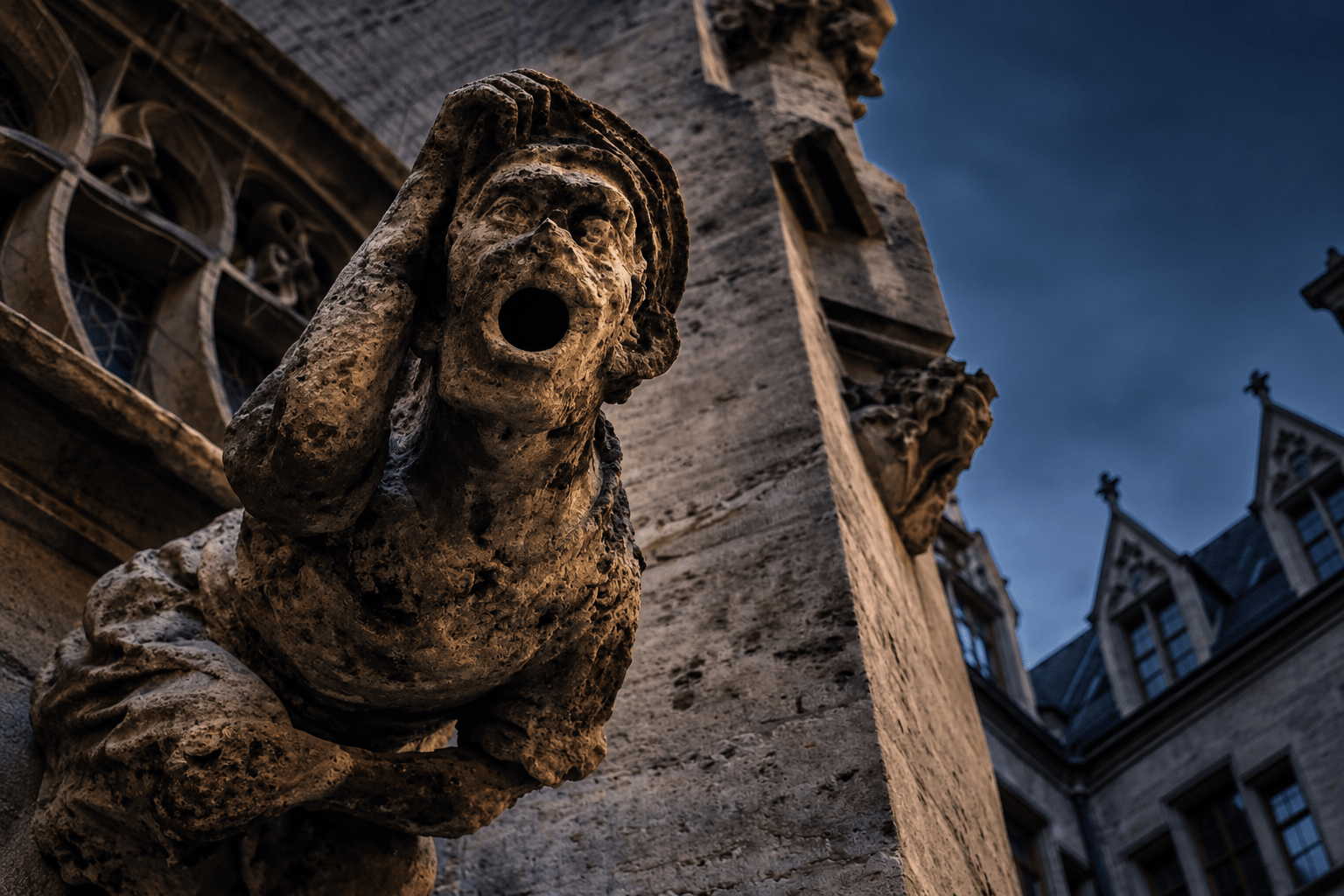 Stone gargoyle on building facade with dramatic clouds in background.