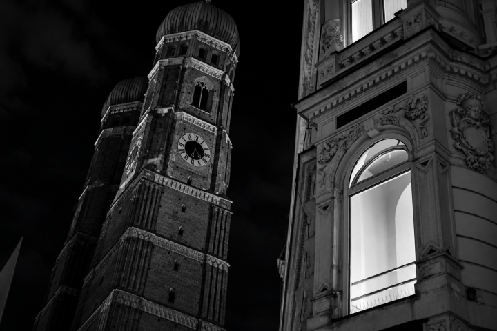Black and white photo of a tall clock tower and a nearby building at night.
